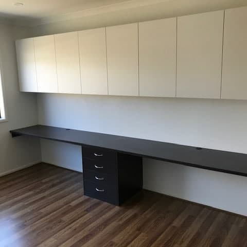 long built in brown study desk with white overhead cabinets
